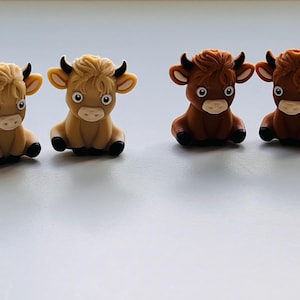 May include: Four small, hand-painted ceramic figurines of cows. Two are brown and two are light brown. The cows are sitting with their legs tucked under them and have black eyes and noses.