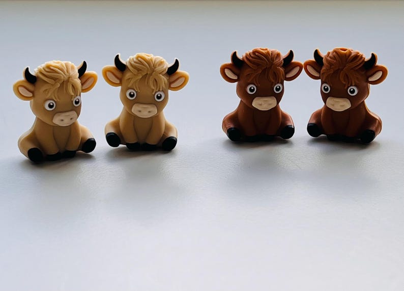 May include: Four small, hand-painted ceramic figurines of cows. Two are brown and two are light brown. The cows are sitting with their legs tucked under them and have black eyes and noses.