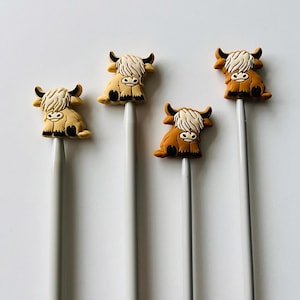 May include: Four knitting needles with cute highland cow toppers. Two of the toppers are brown and two are beige.