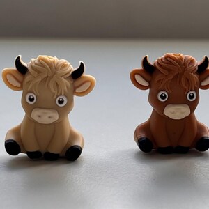 May include: Four small, cartoon-style figurines of cows. Two are brown and two are tan. They are all sitting with their legs tucked under them and have big eyes and a friendly expression.
