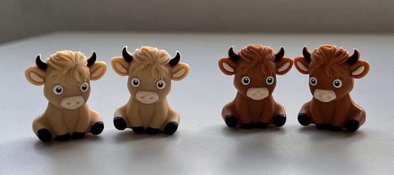 May include: Four small, cartoon-style figurines of cows. Two are brown and two are tan. They are all sitting with their legs tucked under them and have big eyes and a friendly expression.