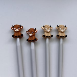 May include: Four knitting needles with animal-shaped tops. Two needles have brown cow tops and two needles have tan cow tops. The needles are silver.