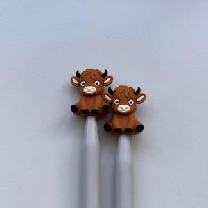 May include: Two brown cow-shaped knitting needle tips on a pair of gray knitting needles.