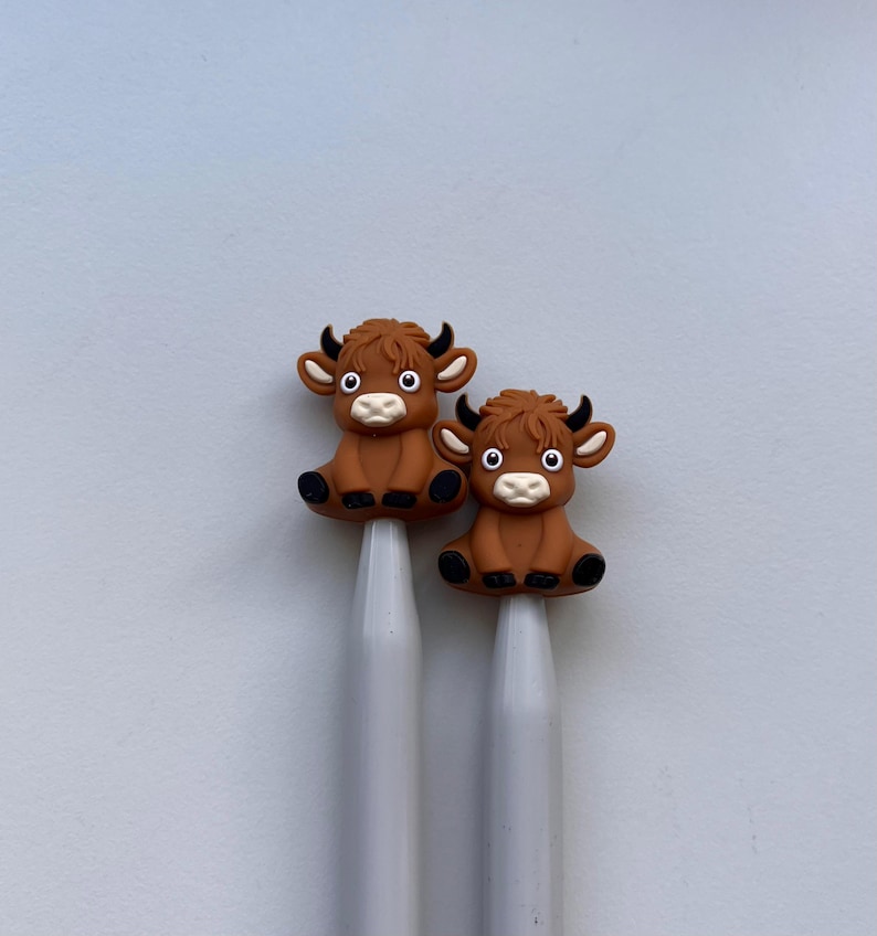 May include: Two brown cow-shaped knitting needle tips on a pair of gray knitting needles.