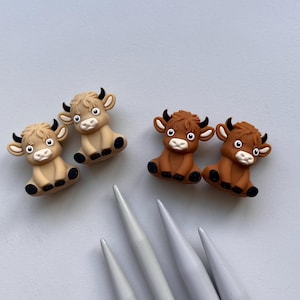 May include: Four small, brown and tan, cow-shaped figurines. The figurines are sitting on a light gray surface.