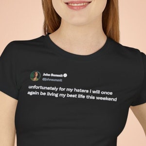 May include: Black cropped t-shirt with a white tweet graphic that reads "unfortunately for my haters i will once again be living my best life this weekend".