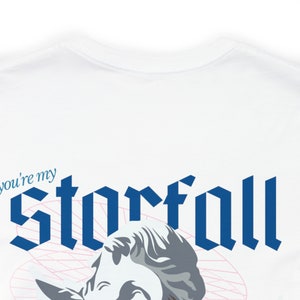 May include: White t-shirt with a blue graphic that says "you're my starfall" in a gothic font. A white and gray sculpture of a woman's head is partially visible below the text.