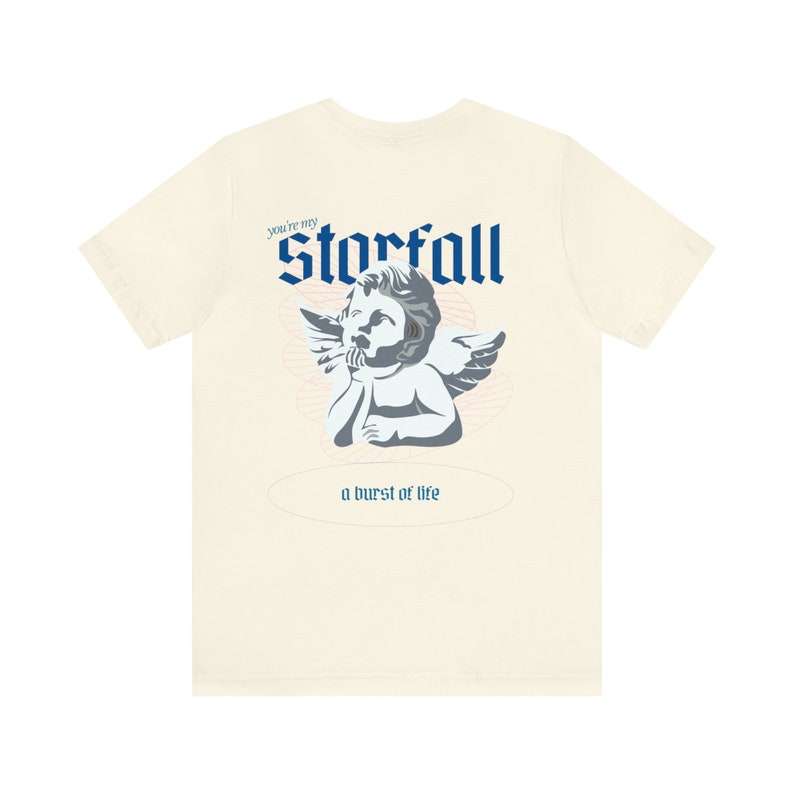 May include: A cream colored t-shirt with a blue graphic of a cherub angel with wings. The text "You're my Starfall" and "a burst of life" are printed on the shirt.