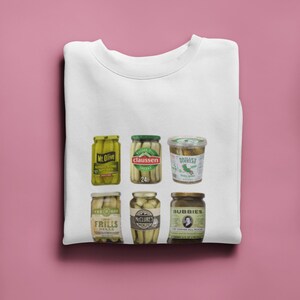 Peut inclure: Un t-shirt blanc avec un motif de six bocaux de cornichons diff&eacute;rents. Les bocaux sont &eacute;tiquet&eacute;s "Mr. Olive", "Claussen", "Gherkin Star", "Tee-Hee", "McClure's" et "Bubbie's".