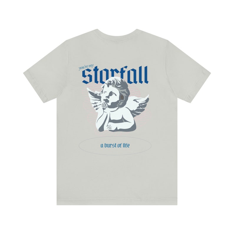 May include: A light gray t-shirt with a blue and white graphic of an angel with the text "You're my Starfall a burst of life" printed on the back.
