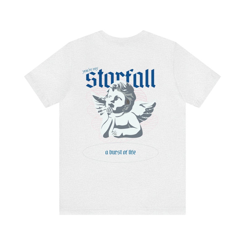 May include: White t-shirt with a blue and gray graphic of a cherub with wings. The text "You're my Storfall" and "a burst of life" are printed on the shirt.