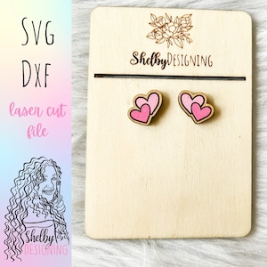 May include: A pair of pink wooden heart earrings on a wooden display card with the text "Shelby DESIGNING".