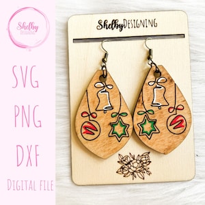 Puede incluir: Un par de pendientes de madera con temática navideña con un diseño de campana, estrella y adorno. Los pendientes están en una tarjeta de exhibición de madera con el texto "Shelby DESIGNING".