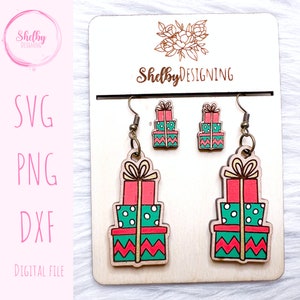 May include: Wooden Christmas-themed earrings and stud earrings set. The earrings and studs are shaped like stacked gift boxes in red, green, and white. The earrings are displayed on a wooden card with the text "Shelby Designing".
