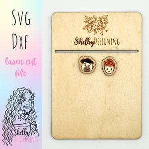 May include: Wooden earrings with cartoon faces of a man and woman are displayed on a wooden card. The card has a slot and the text "Shelby DESIGNING" and "SVG DXF laser cut file". A floral design is above the text.