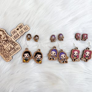 May include: Wooden earrings featuring cartoon characters in various styles. The earrings are in different shapes and sizes, with silver-colored hooks. The image also includes a wooden logo with the text "Shelby Designing" and "SVG DXF LASER CUT FILE".