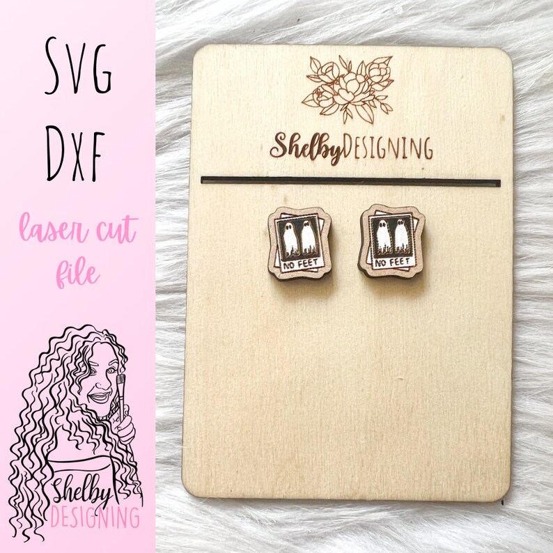 May include: A pair of wooden earrings with a laser-cut design of two ghosts in a photo frame with the text "No Feet". The earrings are displayed on a wooden board with the text "ShelbyDESIGNING".