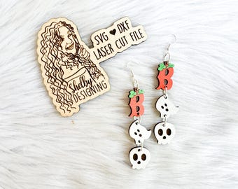 May include: A pair of wooden earrings with a pumpkin and ghost design. The pumpkin is orange with a green stem and the ghost is white with black eyes. The earrings are labeled "SVG ♥ DXF LASER CUT FILE".