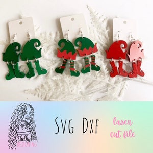 May include: Three pairs of elf-themed earrings, each pair featuring a different colour scheme. The first pair is green, the second is red and green, and the third is red and pink. Each earring features a hat, legs, and boots. The earrings are displayed on white card stock with the text "SVG DXF laser cut file" below.