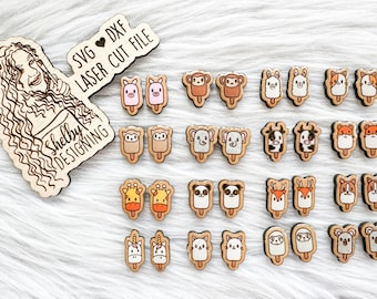 May include: A set of 20 laser cut wooden popsicle earrings featuring various animal designs, including a pig, monkey, llama, cat, owl, elephant, cow, fox, deer, panda, unicorn, and koala. The earrings are arranged in pairs on a white furry surface. The text "SVG ♥ DXF LASER CUT FILE" and "Shelby DESIGNING" are visible on the wooden sign in the top left corner of the image.