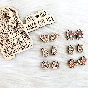 Puede incluir: Un letrero de madera con el texto "SVG ♥ DXF LASER CUT FILE" y las palabras "Shelby Designing" sobre un fondo marrón. El letrero está rodeado de pequeños recortes de madera de animales, incluyendo osos, ardillas, conejos y zorros.