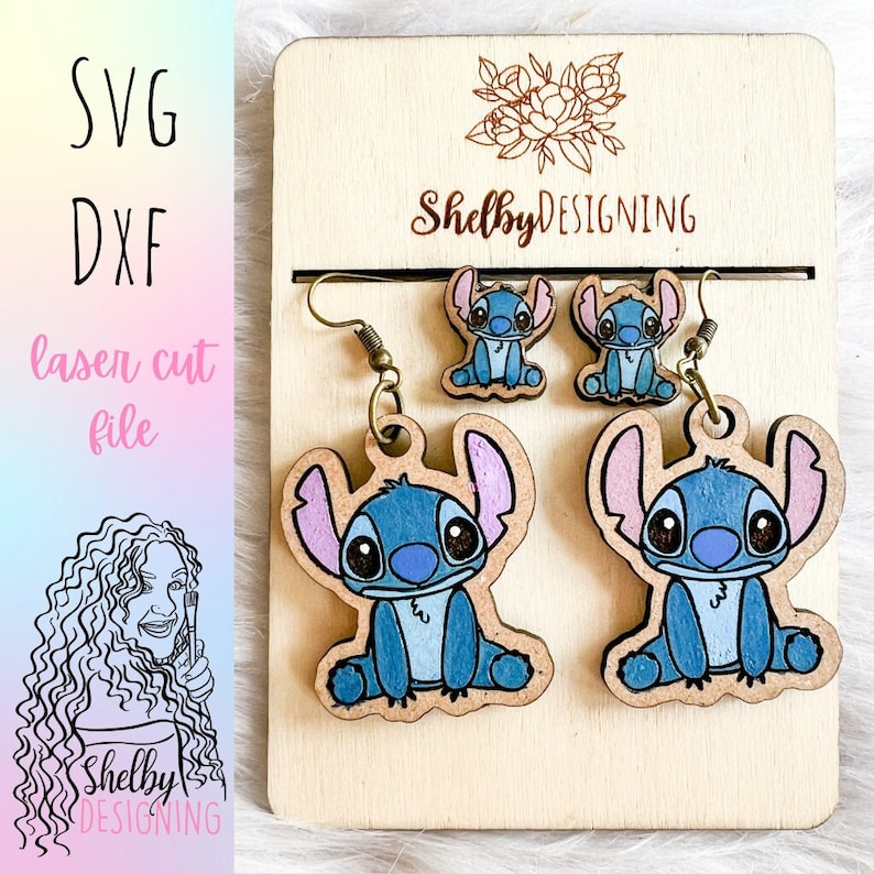 K&ouml;nnte beinhalten: Ein Set aus drei Holzohrringen mit einem blauen Comic-Charakter mit gro&szlig;en Augen und rosa Ohren. Die Ohrringe sind lasergeschnitten und bereit zum Zusammenbauen. Die Ohrringe werden auf einem Holzbrett mit dem aufgedruckten Text "ShelbyDESIGNING" pr&auml;sentiert.