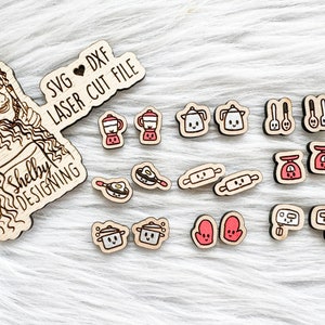 May include: A set of 12 laser cut wooden kitchen themed SVG and DXF files. The files include images of a blender, coffee pot, rolling pin, kitchen scale, pot, oven mitt, and a frying pan. The text "SVG ♥ DXF LASER CUT FILE" and "Shelby Designing" is included on the image.