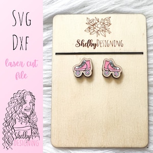 May include: A pair of pink roller skate earrings on a wooden display card. The card has the text "ShelbyDESIGNING" on it.