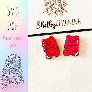 Puede incluir: Dos pendientes rojos con forma de osito de goma, con contornos negros y detalles blancos. Los pendientes están sobre una superficie de madera clara. La imagen también incluye el texto "SVG", "DXF", "laser cut file" y el nombre "Shelby Designing".