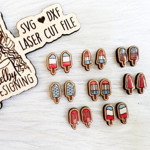 May include: A set of 10 laser cut wooden popsicle earrings. The popsicles are painted in red, white, and blue with a star pattern. The earrings are perfect for summer and patriotic celebrations.