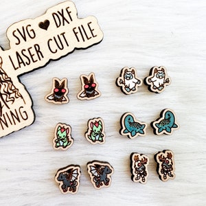 Puede incluir: Un conjunto de 10 pendientes de madera cortados con láser que presentan varios personajes de dibujos animados. Los pendientes son de varios colores, incluyendo azul, verde, rojo y negro. El texto "SVG ♥ DXF LASER CUT FILE" es visible en la esquina superior izquierda de la imagen.