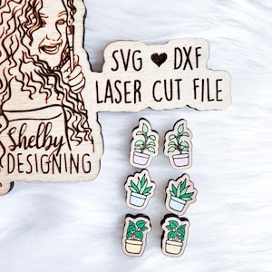May include: SVG ♥ DXF Laser Cut File. Six small wooden cutouts of potted plants with different colored pots and green leaves. The cutouts are on a white surface.