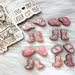 May include: A set of 12 laser cut wooden cutouts in pink. The cutouts include cowboy hats and boots. The cutouts are on a white fuzzy surface. The text "SVG ♥ DXF LASER CUT FILE" and "Shelby DESIGNING" are on the wooden cutouts.
