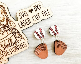 May include: A pair of laser cut wooden earrings featuring a baseball and a baseball glove. The baseball is white with red stitching and the glove is brown with white stitching. The earrings are on a white wooden surface.