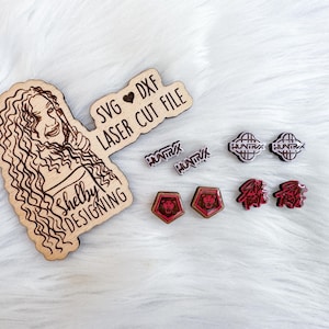 Pode incluir: Arquivo de corte a laser em madeira com um retrato de mulher e o texto "Shelby Designing". Inclui várias peças decorativas pequenas cortadas a laser em vermelho e preto com a palavra "HUNTRX".