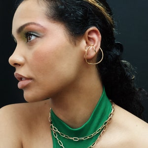 May include: A woman wearing a green halter top with a gold chain necklace and gold hoop earrings.