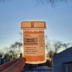 May include: A sticker of a pill bottle with the text "WEENIES 22423 Good Riddance GRACIE ABRAMS AKA: TEHEGRACIETEHE Listen to one song every 6 hours as needed for anxiety Important Information May cause excessive crying May increase your will to live Do not listen if you are at risk of heartbreak"