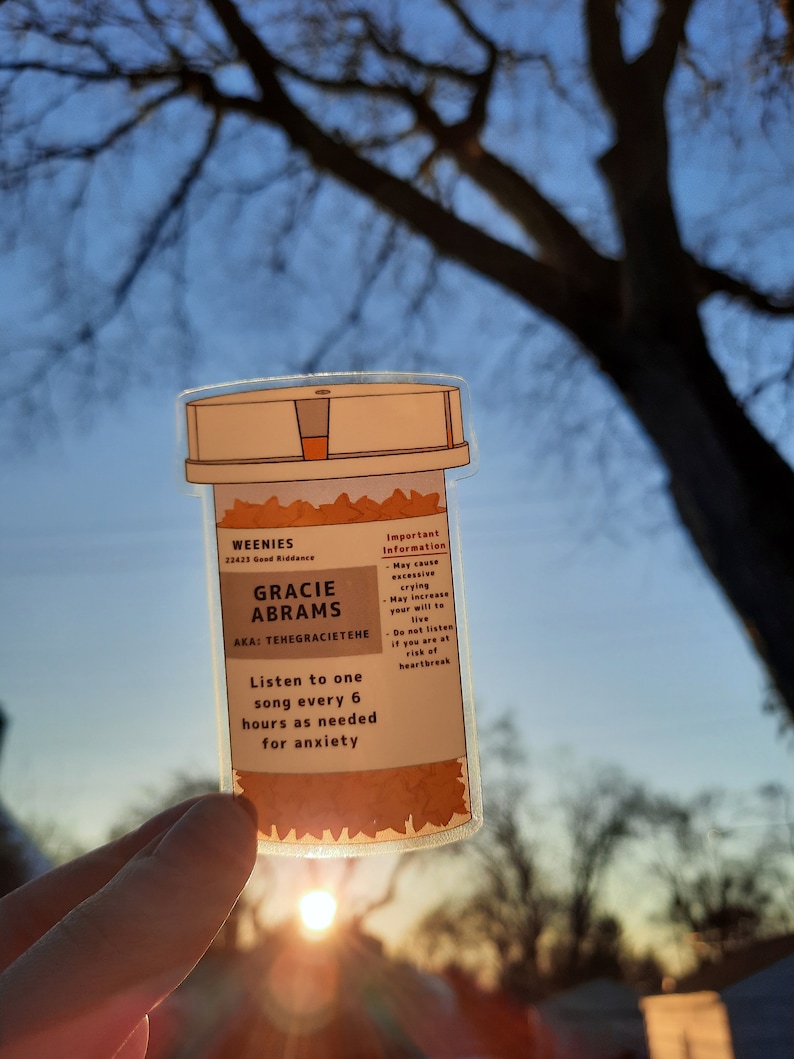 May include: A clear plastic pill bottle with a brown label that reads "WEENIES 22423 Good Riddance GRACIE ABRAMS AKA: TEHEGRACIETEHE Listen to one song every 6 hours as needed for anxiety Important Information - May cause excessive crying - May increase your will to live Do not listen if you are at risk of heartbreak"