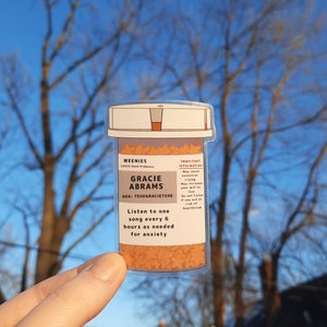 May include: A clear plastic pill bottle sticker with a label that reads "WEENIES 22423 Good Riddance GRACIE ABRAMS AKA: TEHEGRACIETEHE Listen to one song every 6 hours as needed for anxiety Important Information May cause crying May increase your will to live Do not listen if you are at risk of heartbreak"