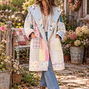 May include: A long, hooded patchwork coat featuring a light blue interior lining with a white cat print. The exterior is composed of various pastel-colored fabric squares in plaid, floral, and solid patterns, including two large front pockets.