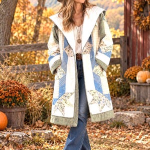 May include: A long, hooded coat featuring a patchwork design with white, blue, and floral fabric squares arranged in star patterns. The coat has a white interior lining and a textured, sage green trim along the edges, front opening, and cuffs.