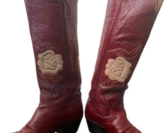 May include: A pair of knee-high red leather cowboy boots with white embroidered roses on the side.