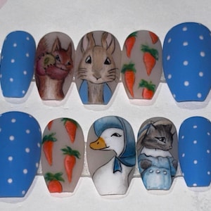 Può includere: Un set di dieci unghie finte blu opache con pois bianchi e illustrazioni dipinte a mano. Le illustrazioni raffigurano uno scoiattolo, un coniglio, carote, un'anatra e un gatto, il tutto in stile libro di fiabe.