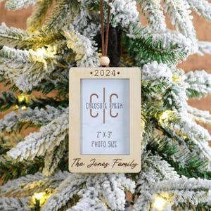 May include: A wooden Christmas ornament with a photo frame, the text "•2024•", "CREOSOTE CREEK", "2" x 3" PHOTO SIZE", and "The Jones Family".