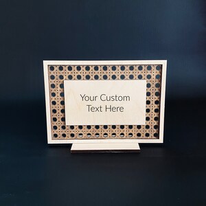Op de afbeelding: Een houten bord met een geweven patroon en een lege ruimte voor tekst. De tekst op het bord luidt "Your Custom Text Here".