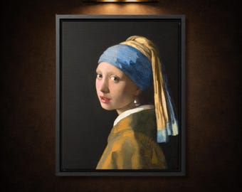 May include: A framed wall art print depicting a portrait of a person wearing a blue headscarf and a yellow garment, featuring a prominent pearl earring. The subject is shown in profile against a dark background, illuminated by a gold light fixture.