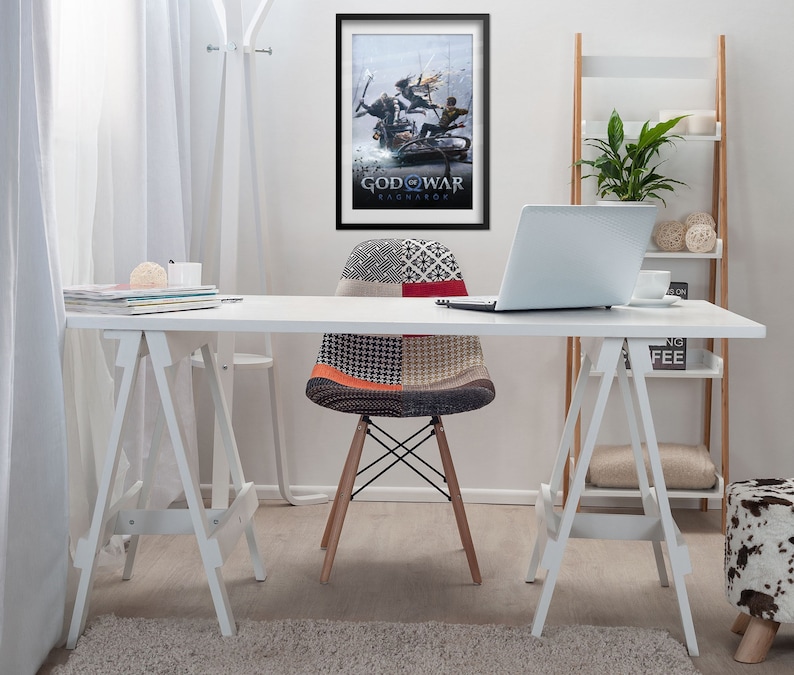 Op de afbeelding: Een wit bureau met een witte stoel en een laptop. Aan de muur achter het bureau hangt een ingelijste poster van de videogame "God of War Ragnarok". De poster toont een sc&egrave;ne waarin Kratos en Atreus vechten tegen een gigantische wolf.