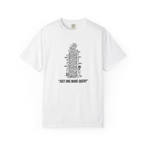 May include: A white short-sleeve t-shirt featuring a black line art graphic of a person peeking out from behind a tall, precarious stack of papers. The text "JUST ONE MORE QUERY" is printed in black capital letters below the illustration.
