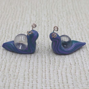 May include: Two small purple and teal snail figurines with clear glass shells and wire antennae.