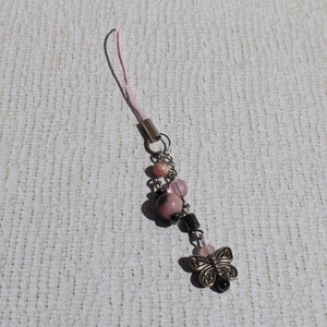 May include: A pink and silver charm with a butterfly pendant and pink and black beads. The charm is attached to a pink string.